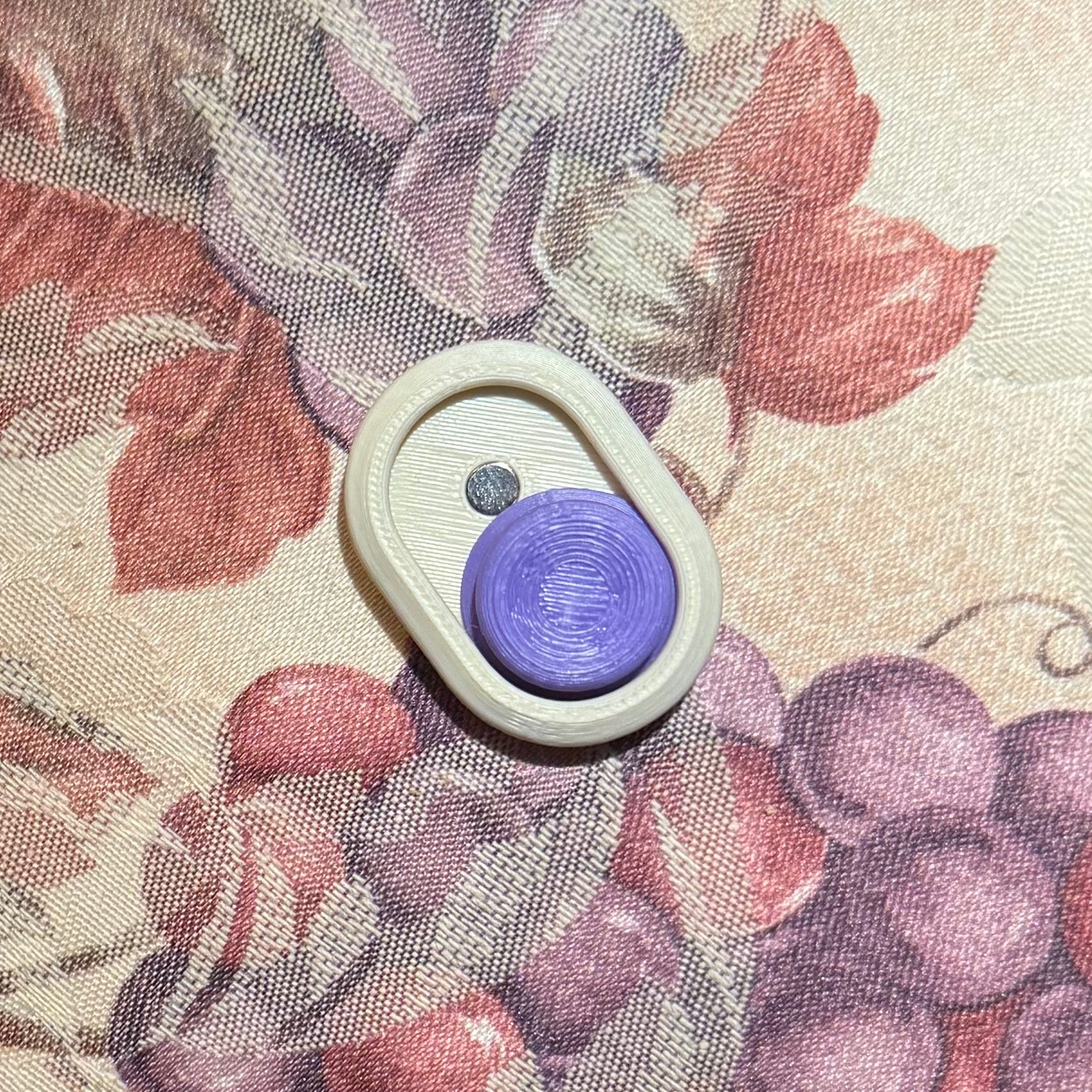 Snappy™ Hidden Gem Clicker Snappy Click style featuring a tactile purple button, perfect for stress relief and focus. Handcrafted executive toy on floral surface.