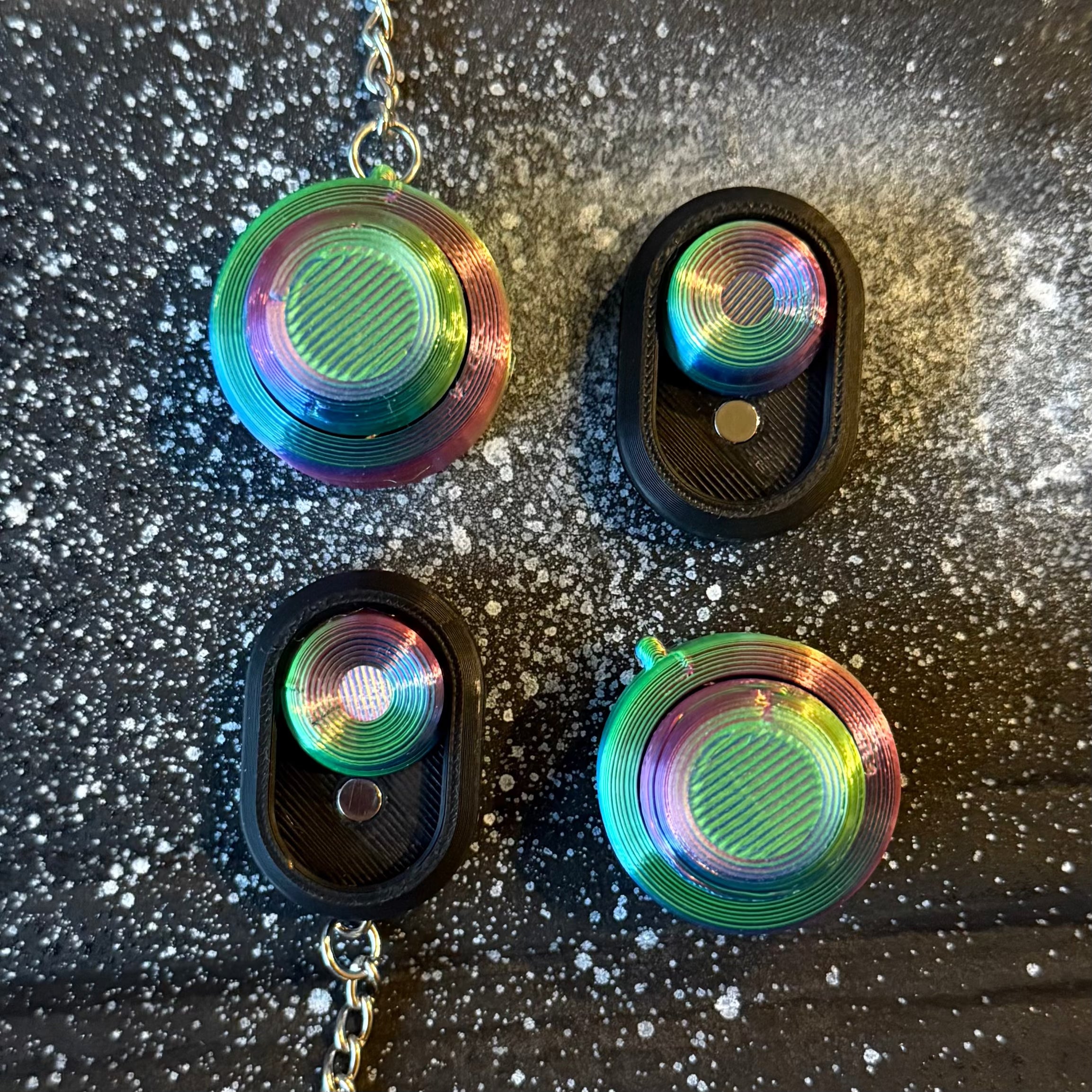Snappy™ Northern Lights Keychain set featuring four aurora-colored fidget toys with metallic rainbow tops and black bases. Ideal for stress relief.