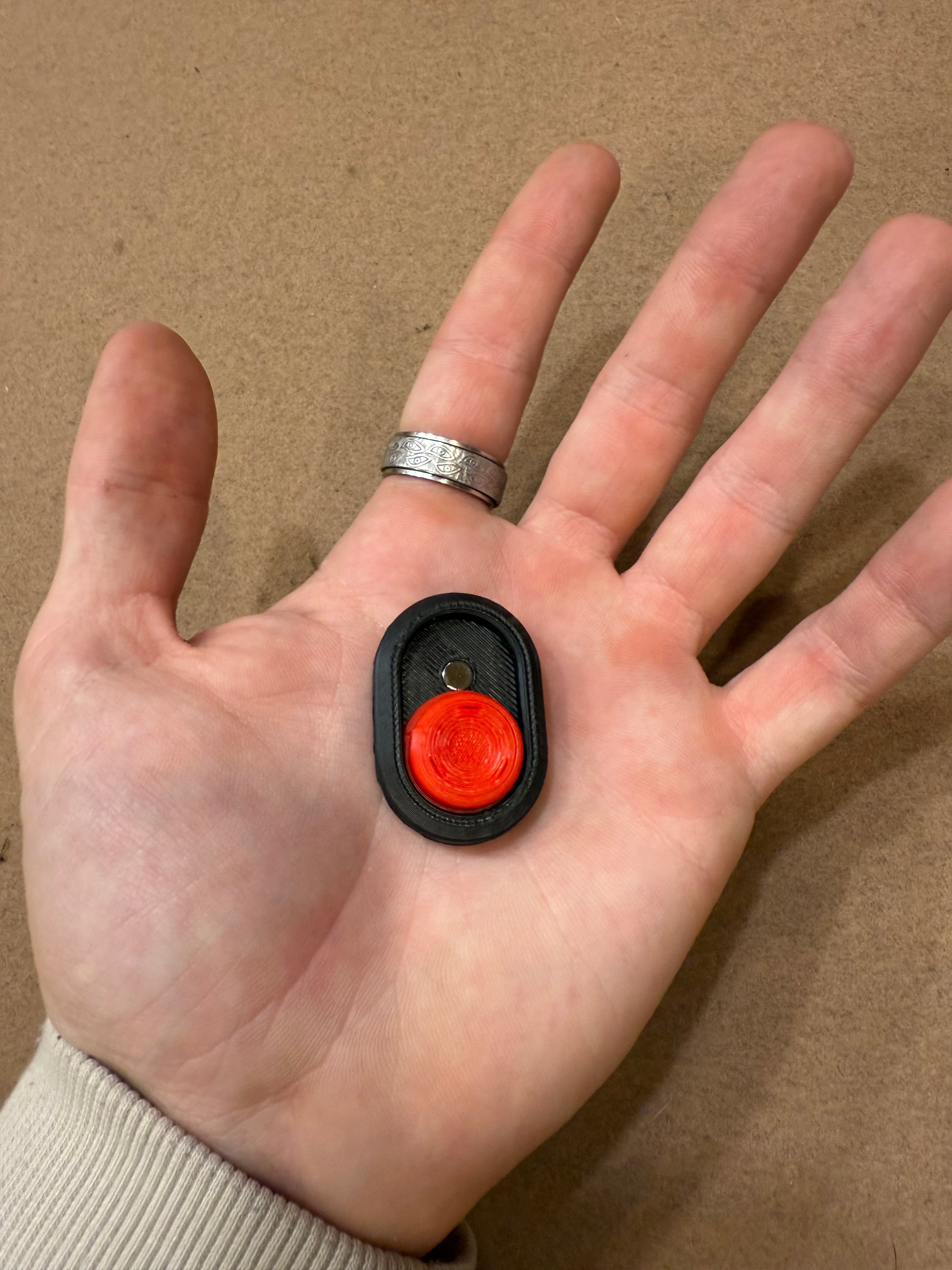 Snappy™ Dragon Eye - Fidget Keyboard Toy shown in hand for scale, featuring a compact red button on a black base for portable stress relief.